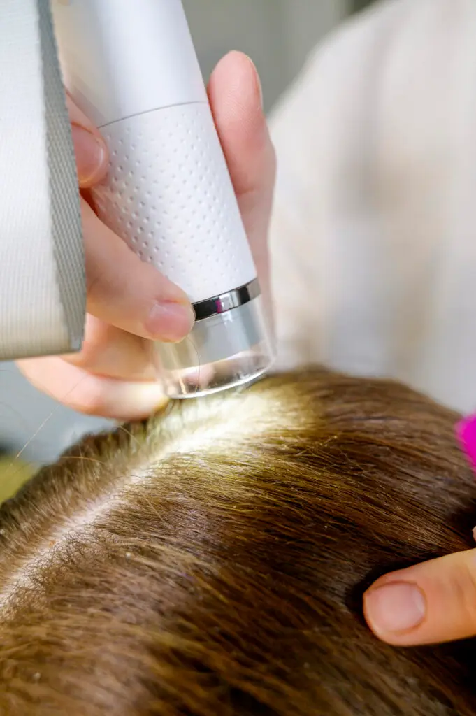 Hand hält ein Analysegerät an die Kopfhaut zwischen den Haaren
